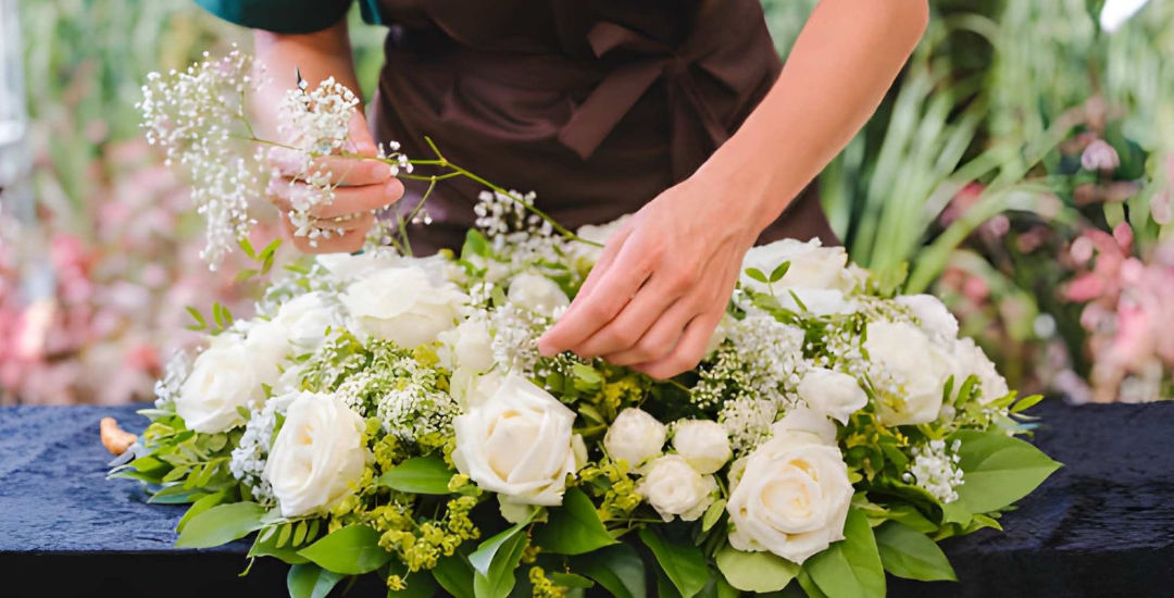 Des mains composent une pièce de deuil blanche en roses et lys dans l'atelier