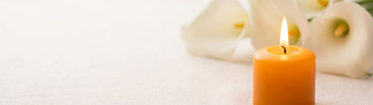 Bougie allumée devant des callas blancs, posées sur une nappe de lin clair