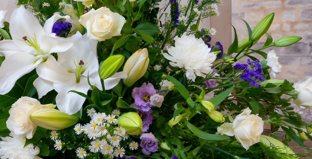 Pièce de fleurs blanches en lys, roses crème et lisianthus, posée contre un mur de pierre