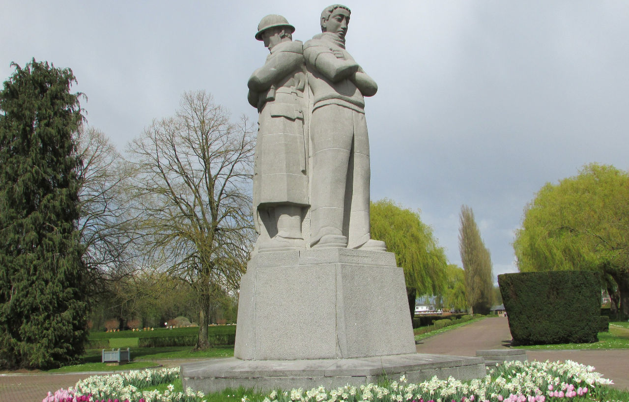 Monument de pierre du cimetière d'Anderlecht, entouré de massifs fleuris.