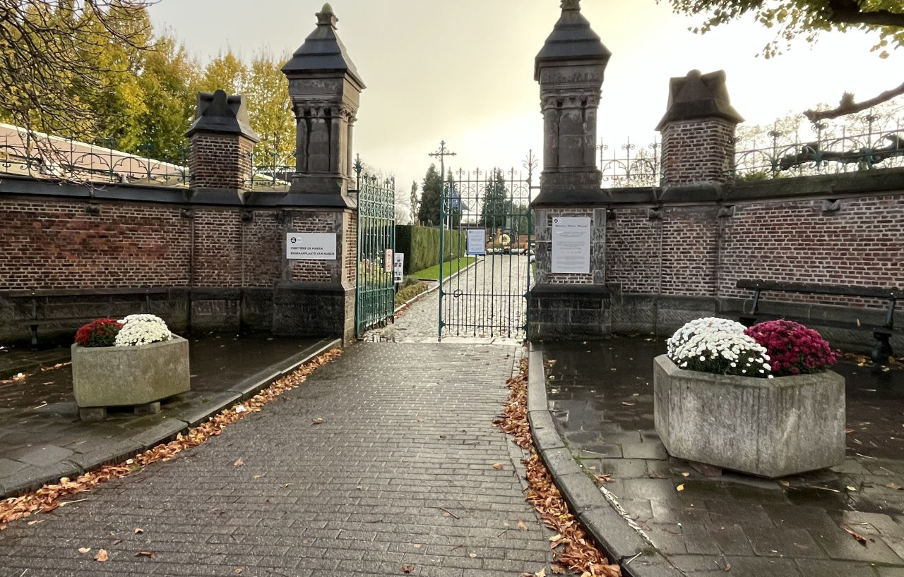 Entrée en brique du cimetière de Haren, avec les jardinières fleuries de part et d'autre de l'allée.