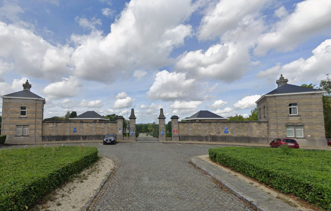 Entrée monumentale du cimetière de Koekelberg, un pavillon de pierre de chaque côté de la grille et des haies taillées devant.