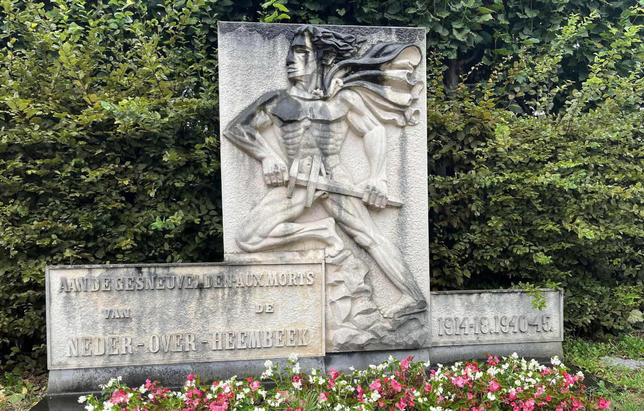 Monument en pierre du cimetière de Neder-Over-Heembeek, devant un massif fleuri.
