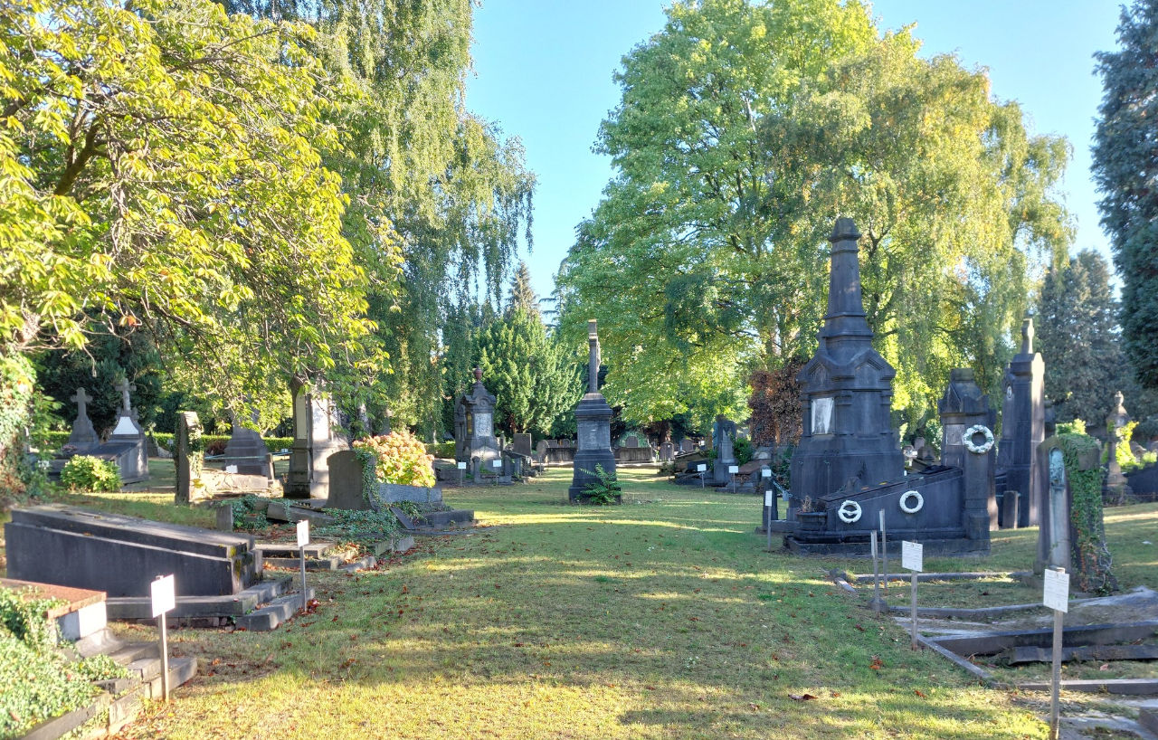Allée du cimetière de Woluwe-Saint-Lambert, bordée de monuments et d'arbres.