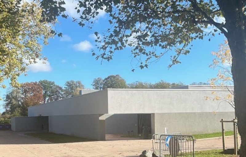 Crématorium d’Evere, bâtiment bas en béton clair entouré de pelouse et d’arbres.