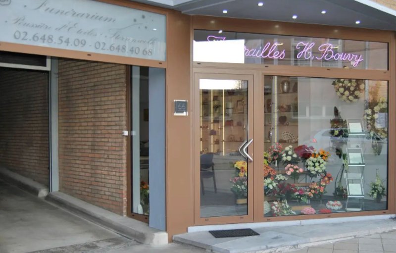 Vitrine des Funérailles Henri Bouvy à Ixelles, enseigne au néon et compositions florales derrière la vitre.