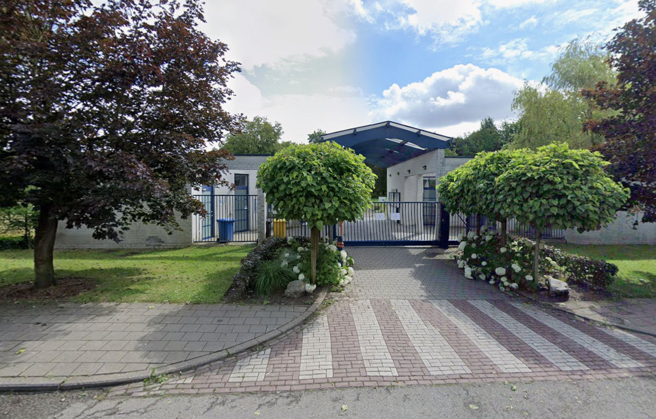 Entrée du nouveau cimetière de Ganshoren, l'auvent bleu du bâtiment d'accueil derrière la grille fermée.