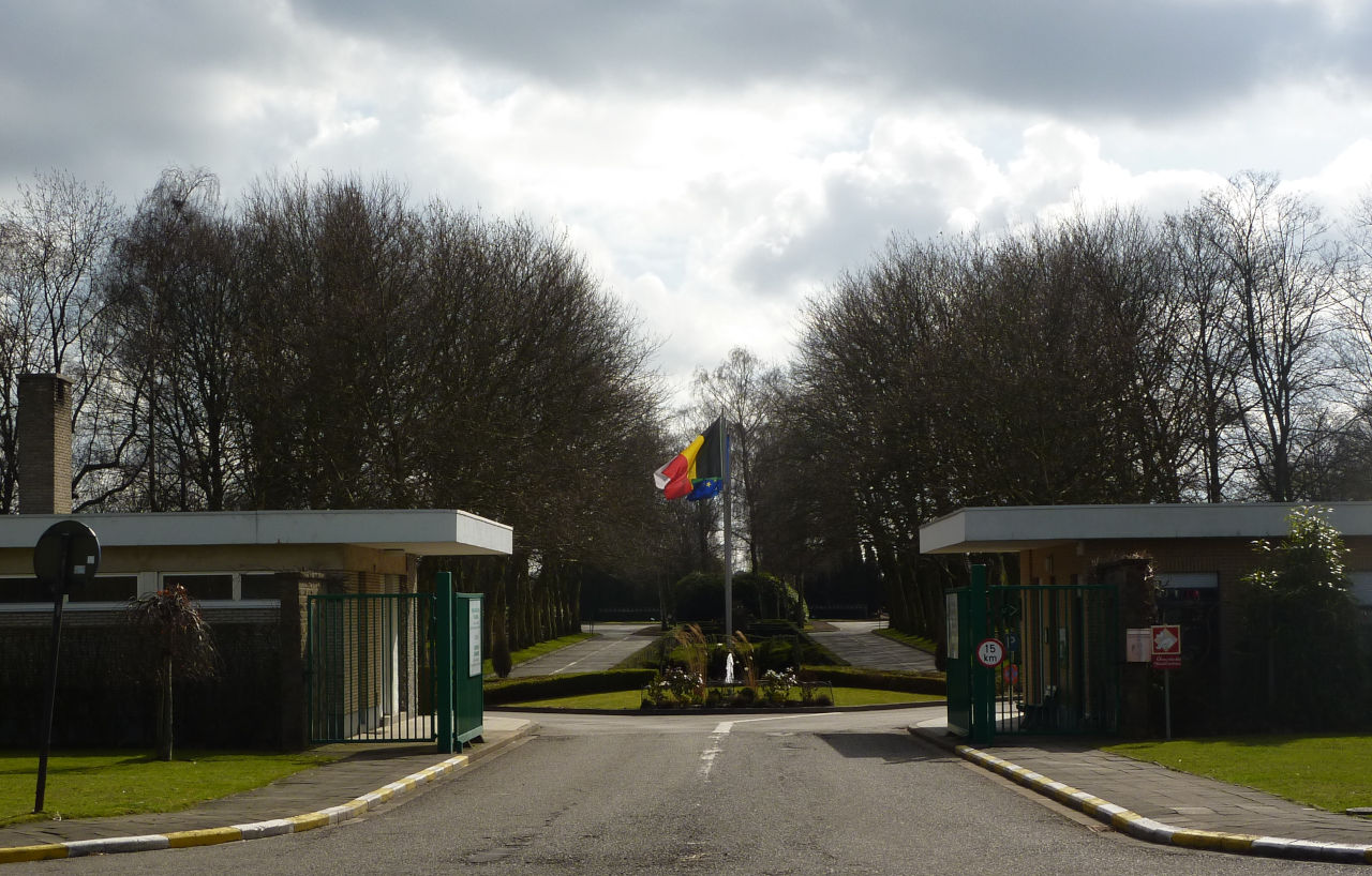 Entrée du Pavillon du Dernier Hommage à Evere, avec les drapeaux et l'allée bordée d'arbres.