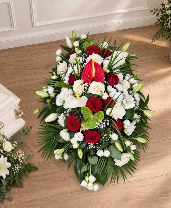 Bûche funéraire roses et anthuriums, allongée en rouge et blanc avec des lys