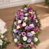 Pièce allongée en lys violets et roses crème Bûche funéraire lys et lisianthus en violet et crème, avec des gerberas