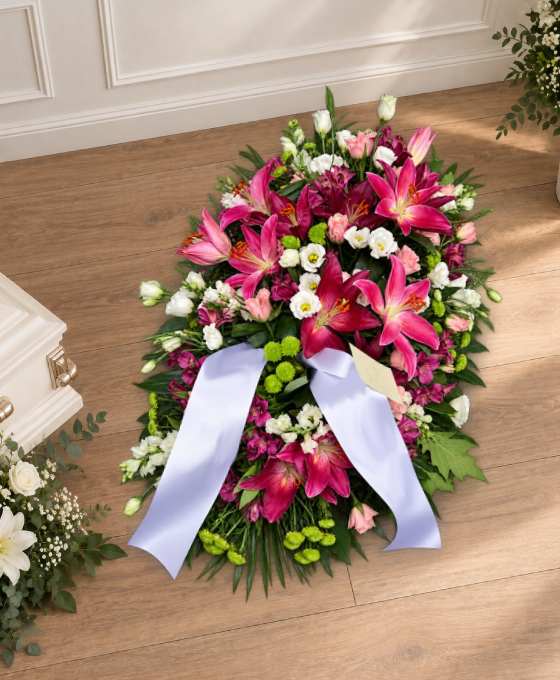 Bûche funéraire fuchsia en lys et roses, avec des chrysanthèmes verts et un ruban
