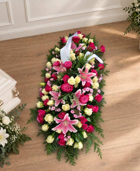 Bûche funéraire en dégradé de rose et fuchsia, en lys et roses avec un ruban