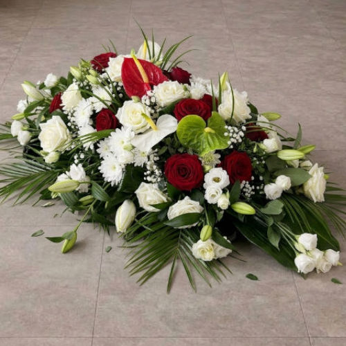 Dessus de cercueil fleuri en roses rouges et blanches, avec chrysanthèmes, anthuriums et palmes, posé au sol