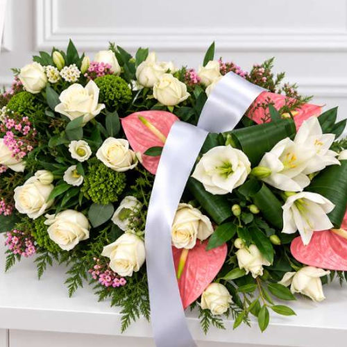 Coussin mortuaire en roses crème, lys blancs et anthuriums roses, avec un large ruban blanc