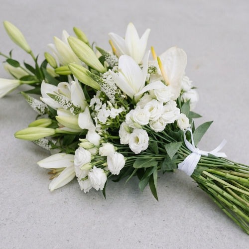 Gerbe funéraire blanche en lys, anthurium et lisianthus, liée par un ruban et posée à plat