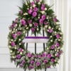 Couronne sur trépied en œillets Couronne mortuaire lilas et mauve en œillets et chrysanthèmes, avec roses blanches et ruban violet