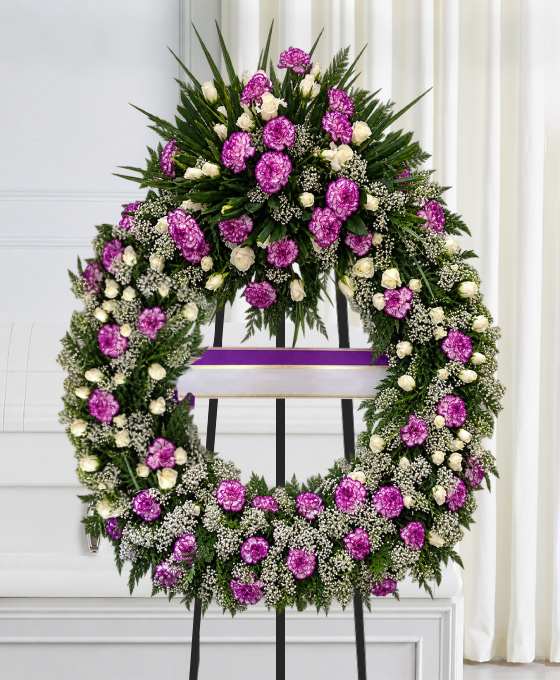 Couronne mortuaire lilas et mauve en œillets et chrysanthèmes, avec roses blanches et ruban violet