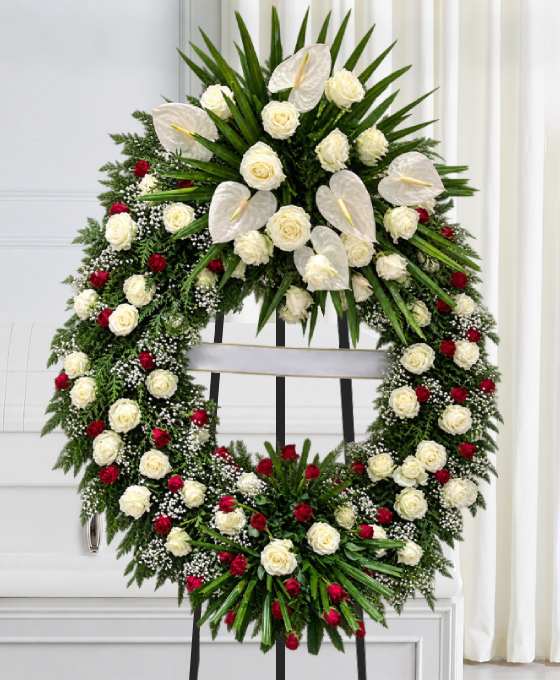 Couronne mortuaire blanche et rouge en roses, avec des anthuriums et des palmes, sur trépied