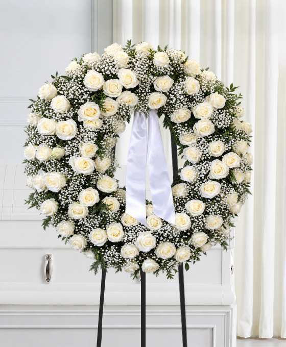 Couronne tout en roses crème et gypsophile, avec un ruban blanc, sur trépied
