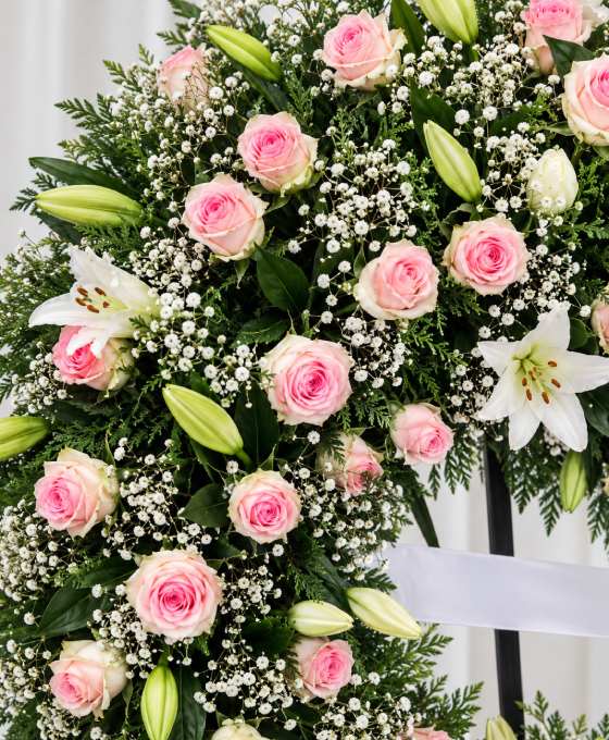 Gros plan : couronne sur trépied en roses roses et crème Gros plan sur les fleurs : couronne sur trépied en roses roses et crème, avec lys blancs et gypsophile