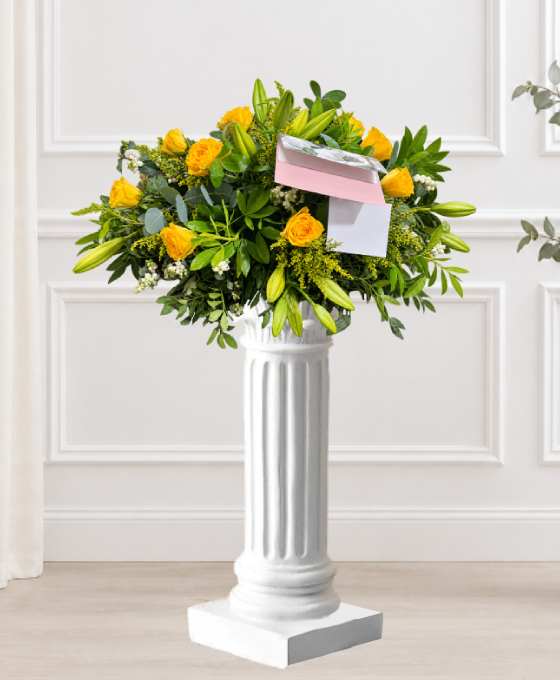 Coussin de roses et lys sur colonne, en jaune avec de la verdure et une carte de condoléances