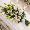 Gerbe blanche posée sur le cercueil Gerbe funéraire blanche en lys, anthurium et lisianthus posée sur un cercueil clair