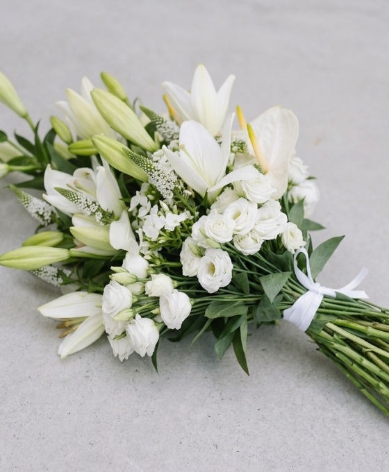 Gerbe funéraire blanche en lys, anthurium blanc, lisianthus et véronique, liée par un ruban