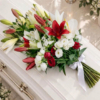 Gerbe rouge et blanche sur le cercueil Gerbe funéraire rouge et blanche en lys et roses posée sur un cercueil clair