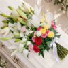 Gerbe de plusieurs couleurs sur le cercueil Gerbe funéraire multicolore en lys blancs et roses jaunes roses et rouges posée sur un cercueil clair